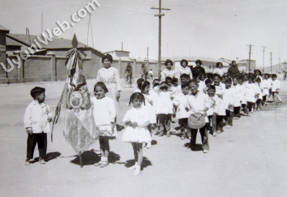 Parade of children with adult women along through a city street.